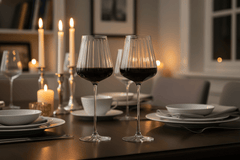 Dining table set with wine glasses, plates, and candles in a cozy indoor setting.