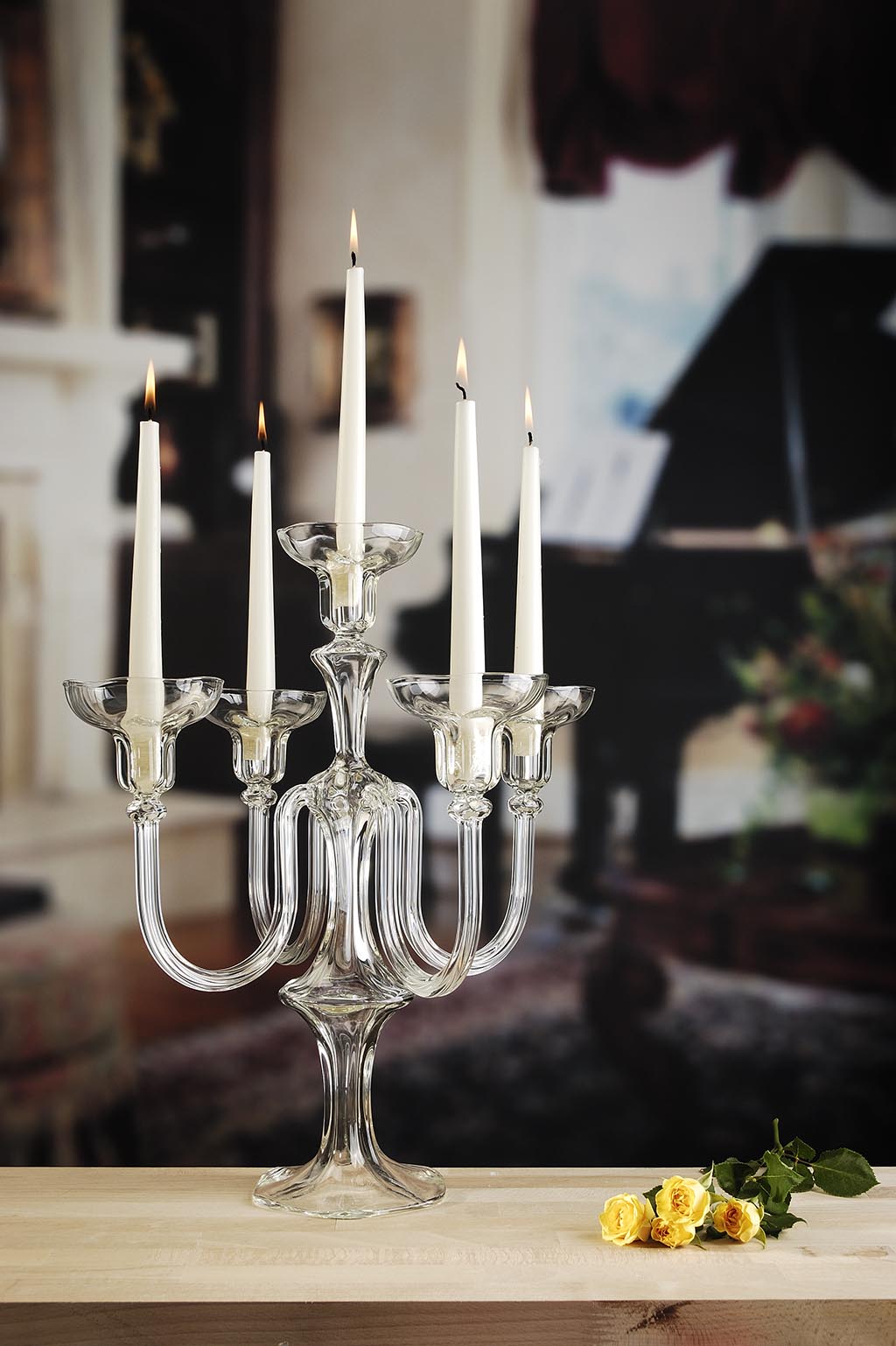 Clear glass candelabra with lit candles on a wooden surface, blurred indoor background