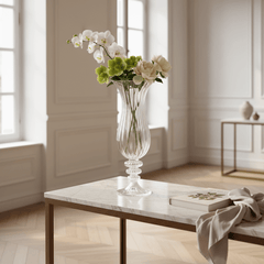 William Vase with white and green flowers on a marble table in an elegant room. Book on table, natural light. Beige walls and hardwood floors.