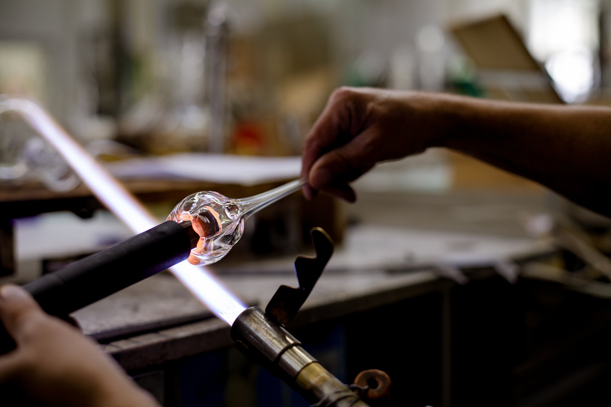 Glassblowing process with a glass object being shaped by a person's hands.